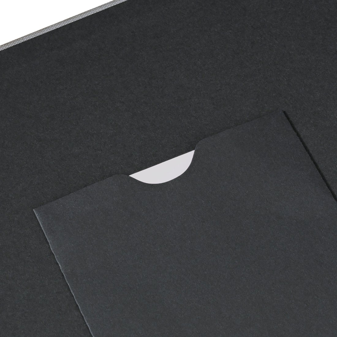 Ciemnoszary notatnik z otworem ukazujäcym biały papier.