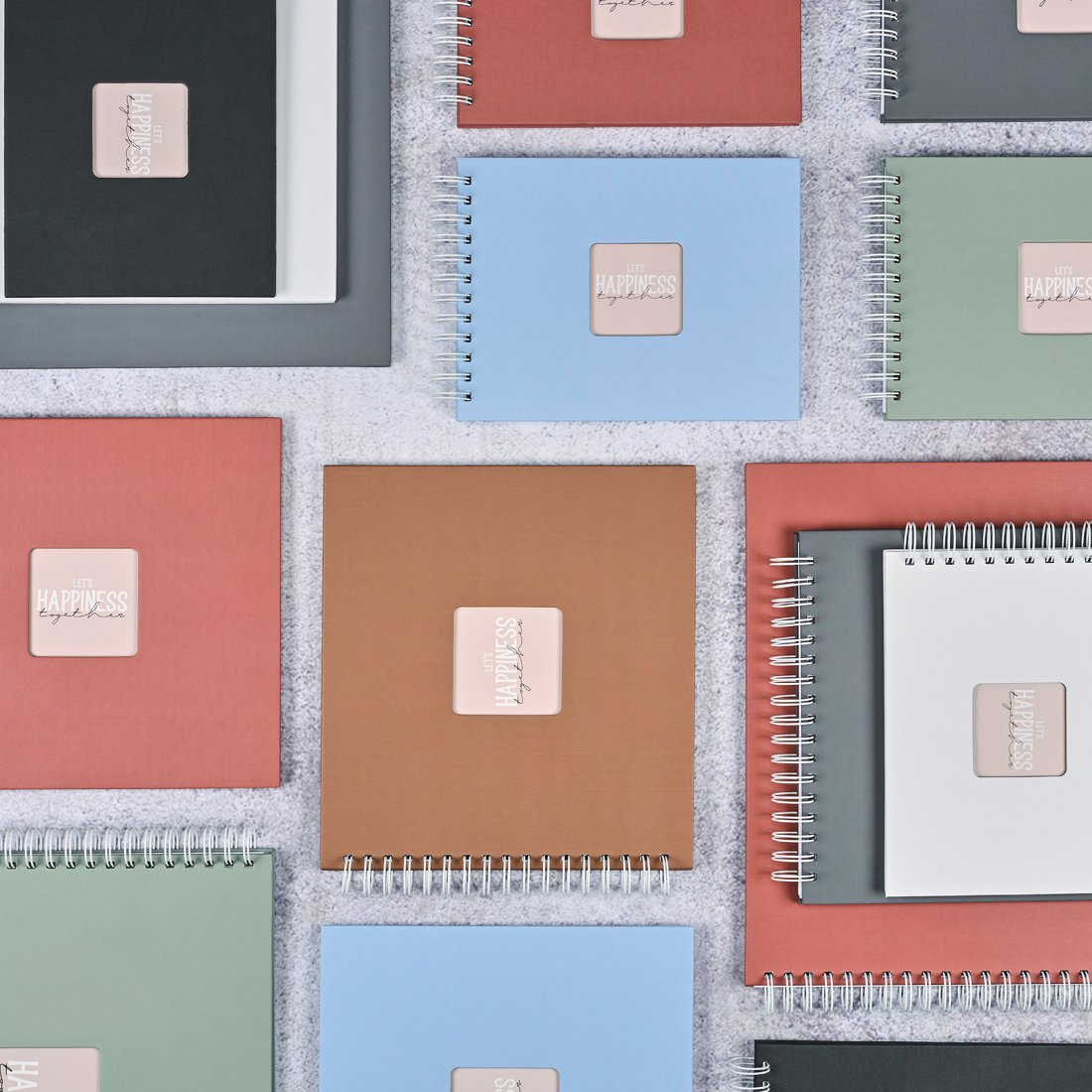 Wiele zeszytów bindowanych spiralnie w różnych kolorach leży na teksturowanej powierzchni.