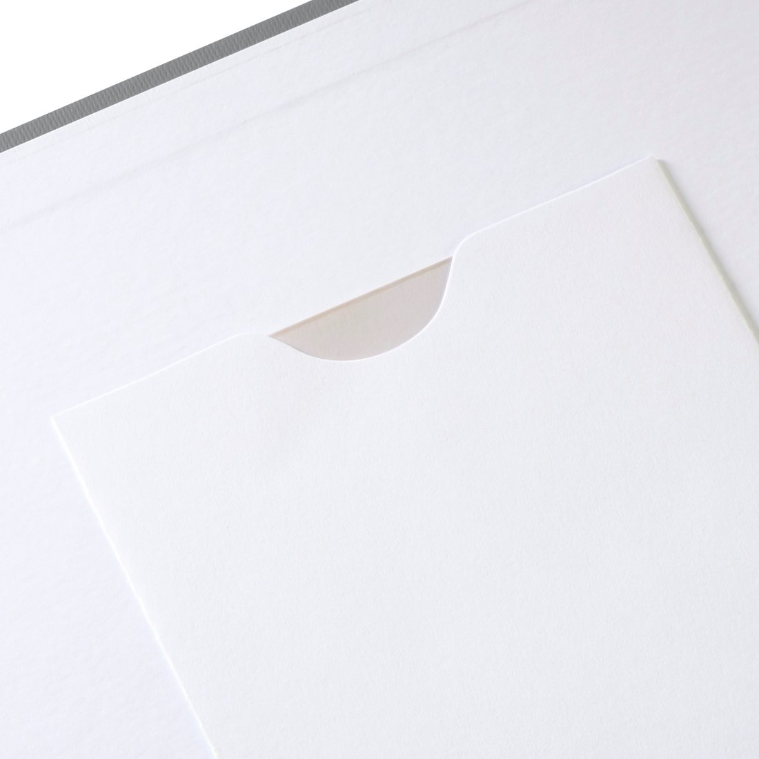 Biały arkusz papieru z wyciętym otworem ukazującym jaśniejszą powierzchnię pod spodem.