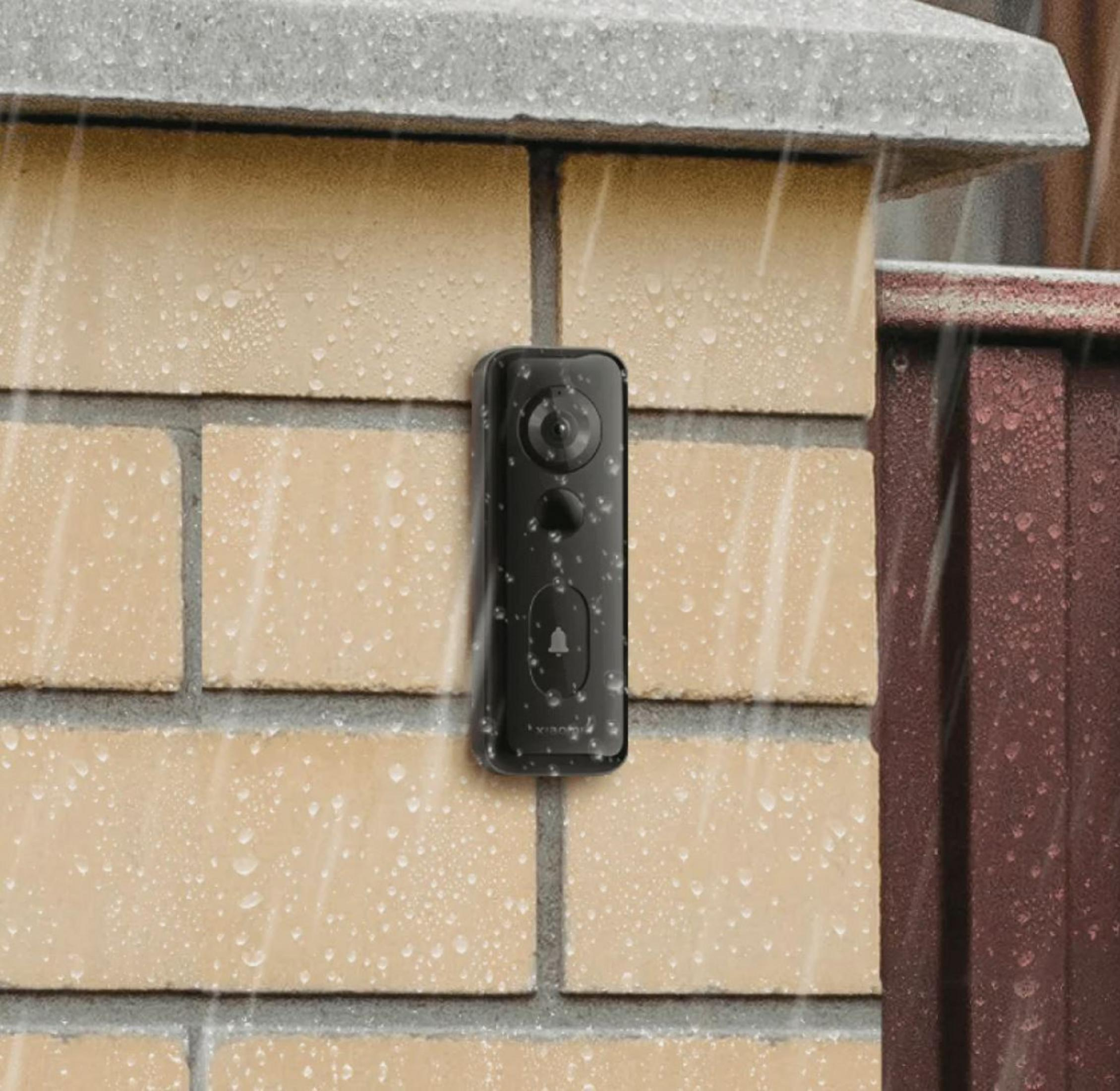Czarny dzwonek do drzwi z kamerą na ceglanym murze w deszczu.