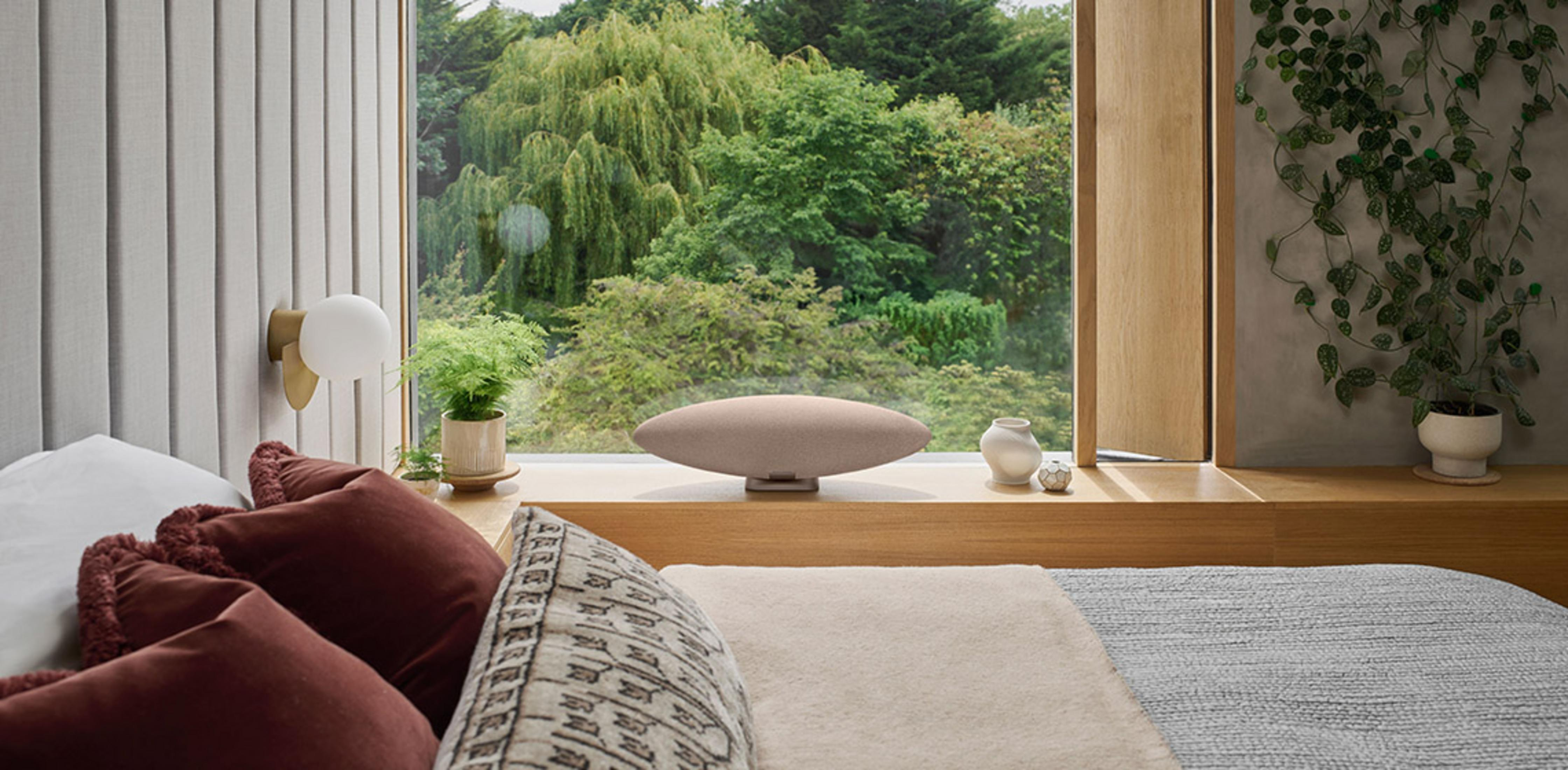 Owalny głośnik stoi na parapecie z widokiem na bujny zielony las.