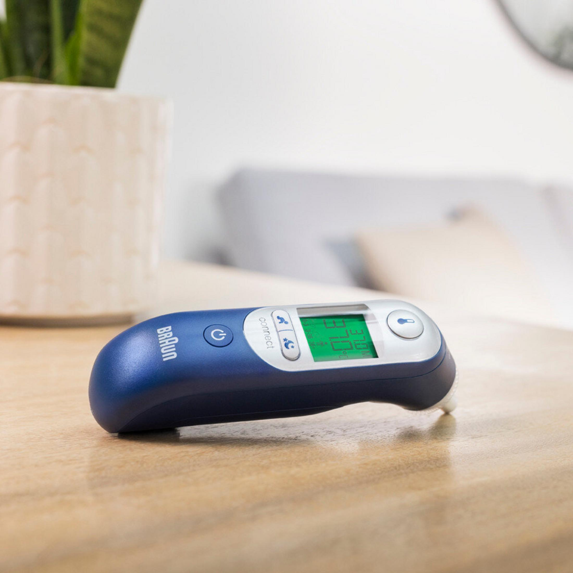 Niebieski termometr Braun z zielonym wyświetlaczem leży na drewnianym stole.