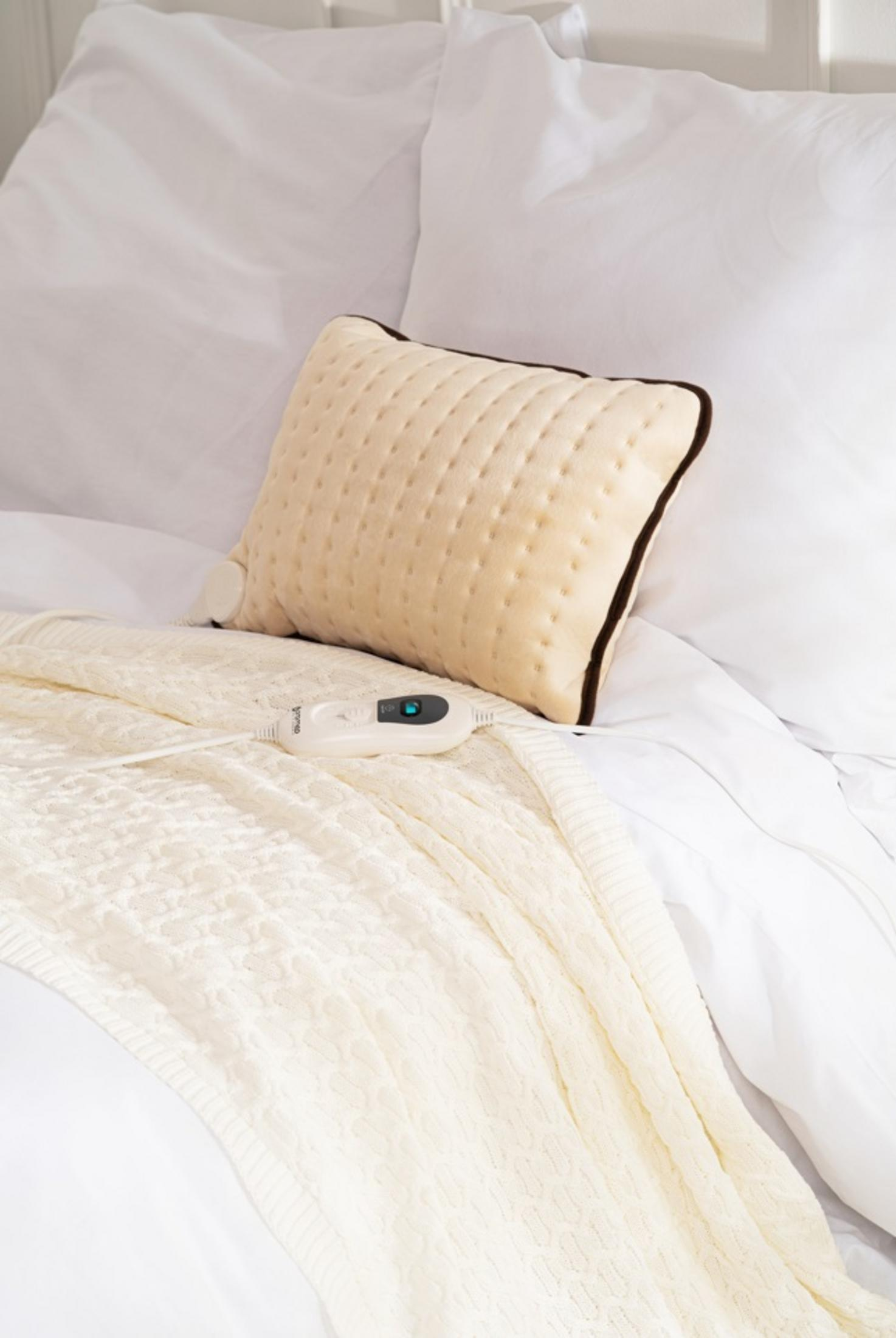 Un termoforo color crema con bordo marrone giace su una coperta.