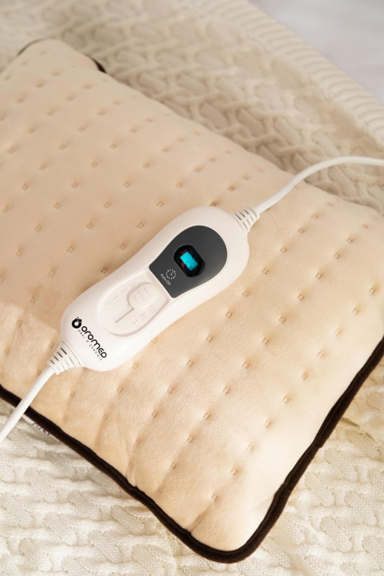Un termoforo beige chiaro con controller e cavo bianchi su una coperta.