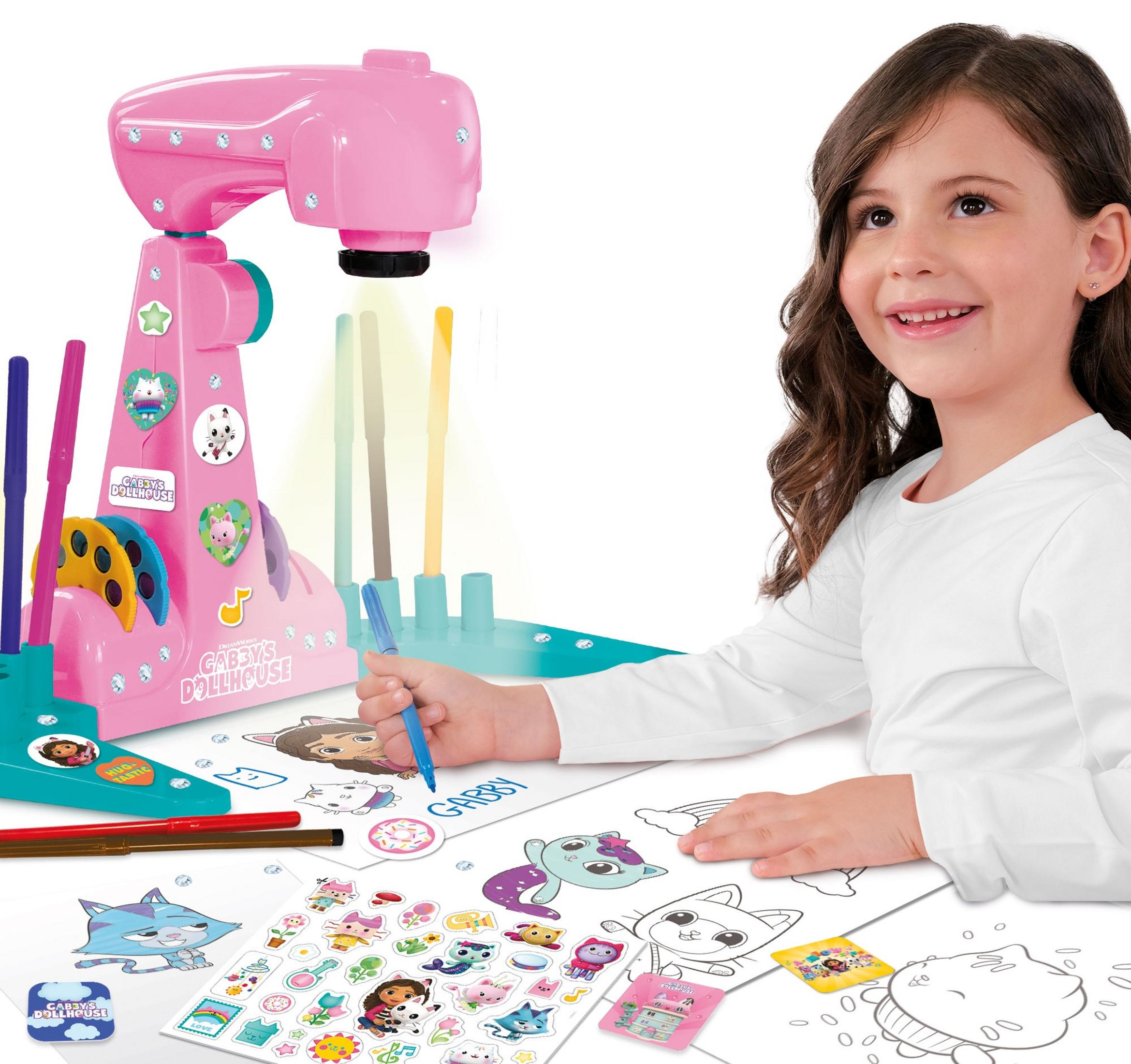 Dziewczynka rysuje niebieskim długopisem na papierze. Obok stoi różowy projektor.