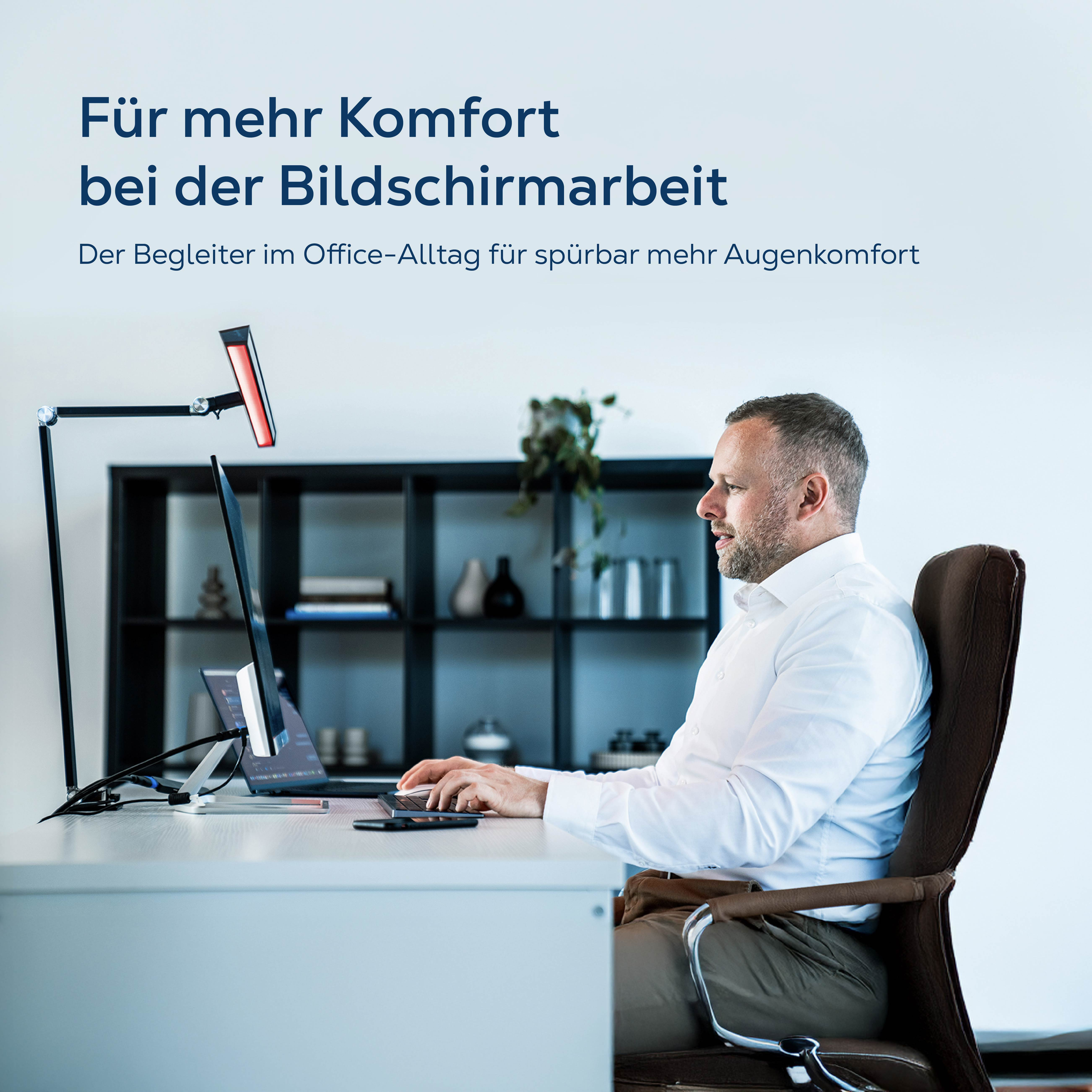 Mann am Schreibtisch, der auf einen Laptop blickt. Ein Monitor ist auf einem Arm montiert.