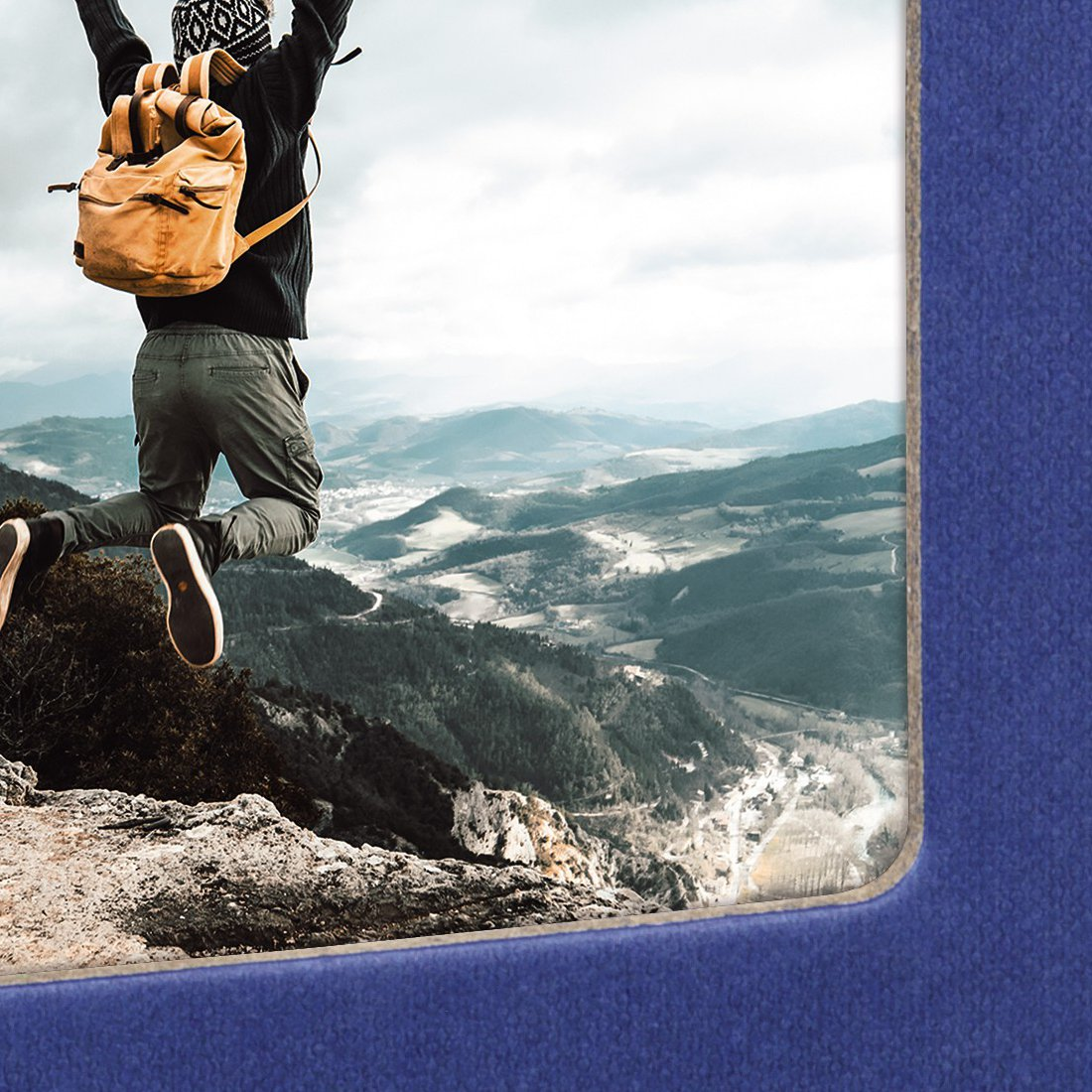 Turysta z plecakiem skacze na górze z widokiem na dolinę.