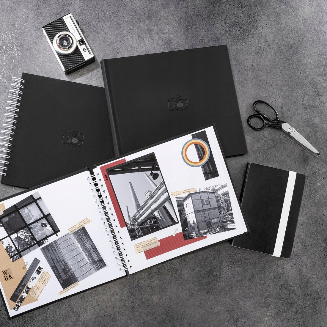 Otwarty album na zdjęcia z aparatem, nożyczkami i notatnikiem na szarej powierzchni.