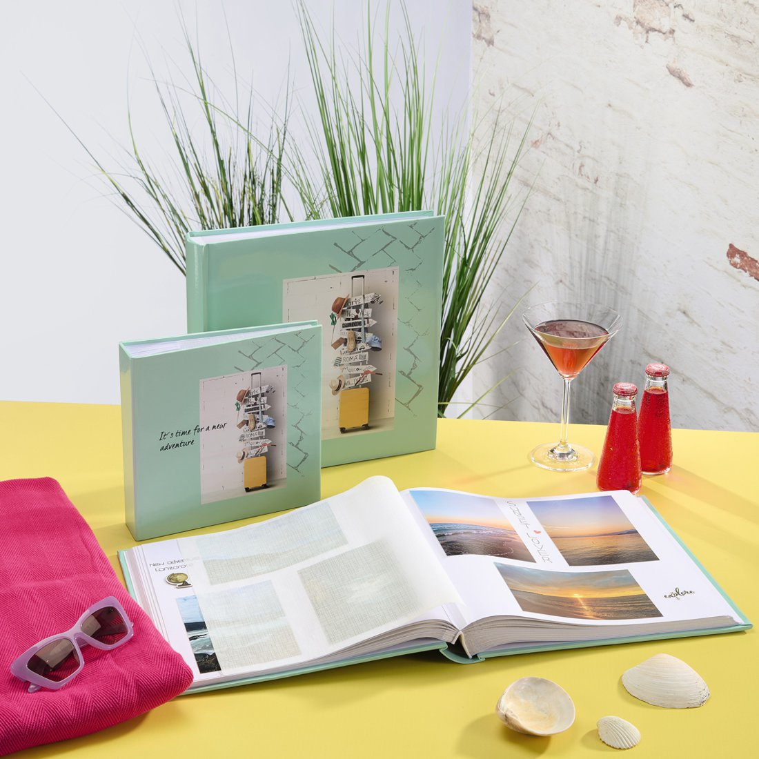 Dwa albumy na zdjęcia, jeden otwarty ze zdjęciami plażowymi, na żółtym stole.