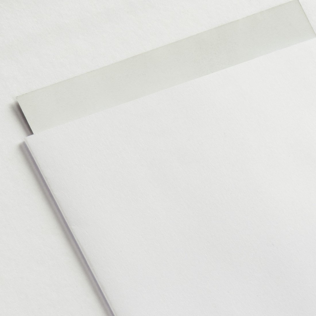 Biała kartka papieru leży na białej powierzchni. Część jest lekko podniesiona.