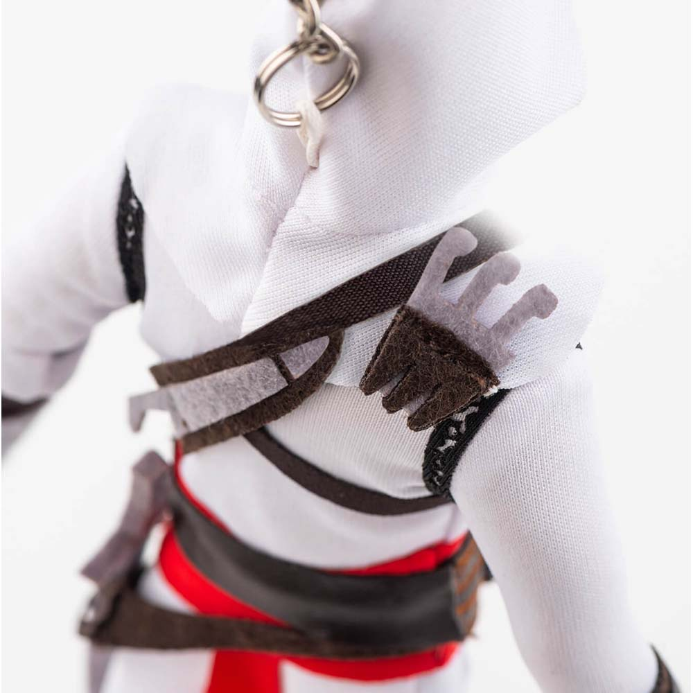 Primo piano di un action figure con cappuccio bianco, cinghie marroni e accento rosso.