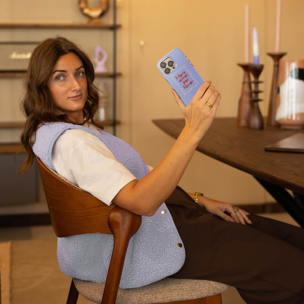 Een vrouw zit in een stoel en houdt een paarse telefoon vast met „More amor por favor“.
