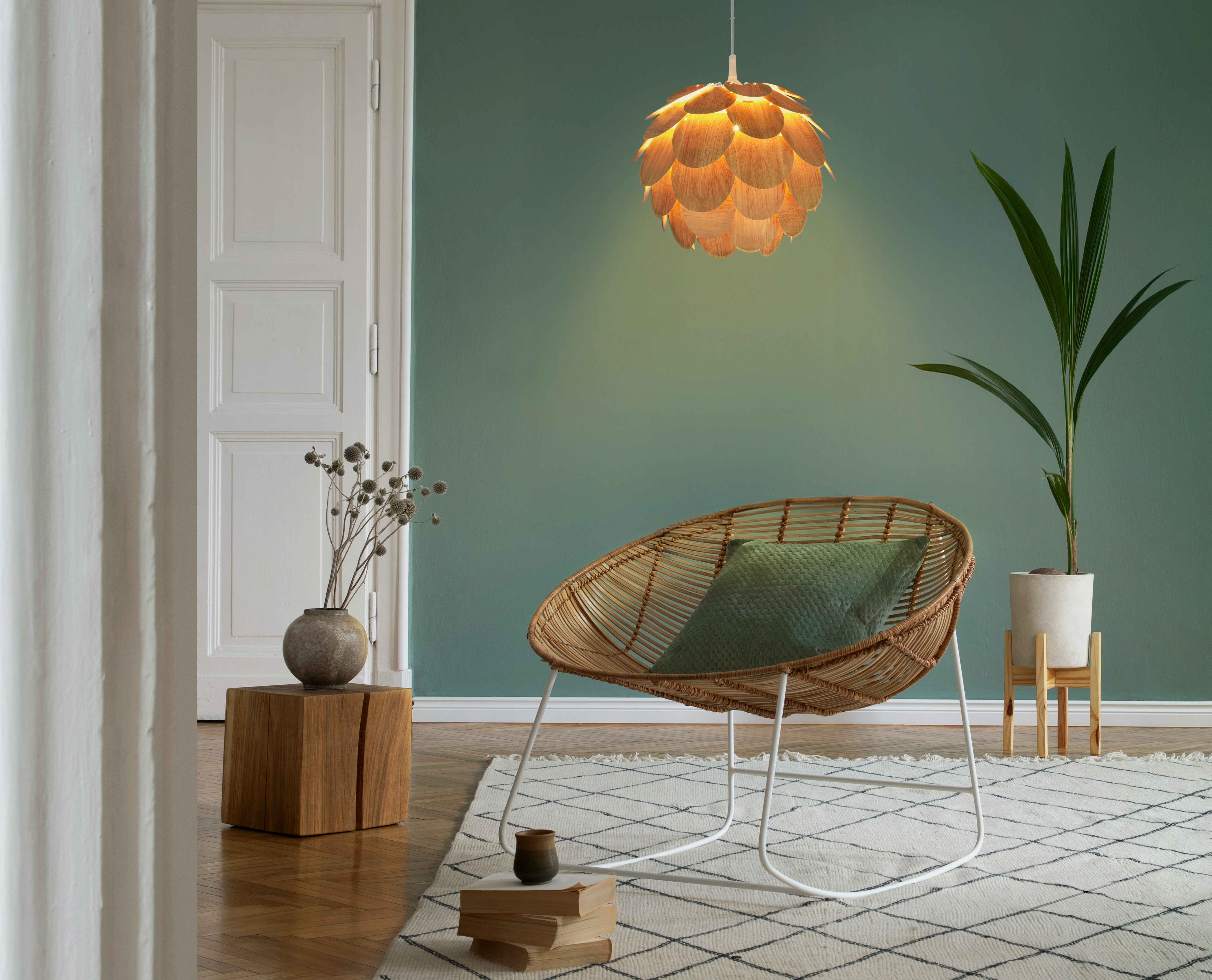 Ein Rattansessel mit Kissen steht auf einem Teppich neben einem Holzwürfel mit Vase.
