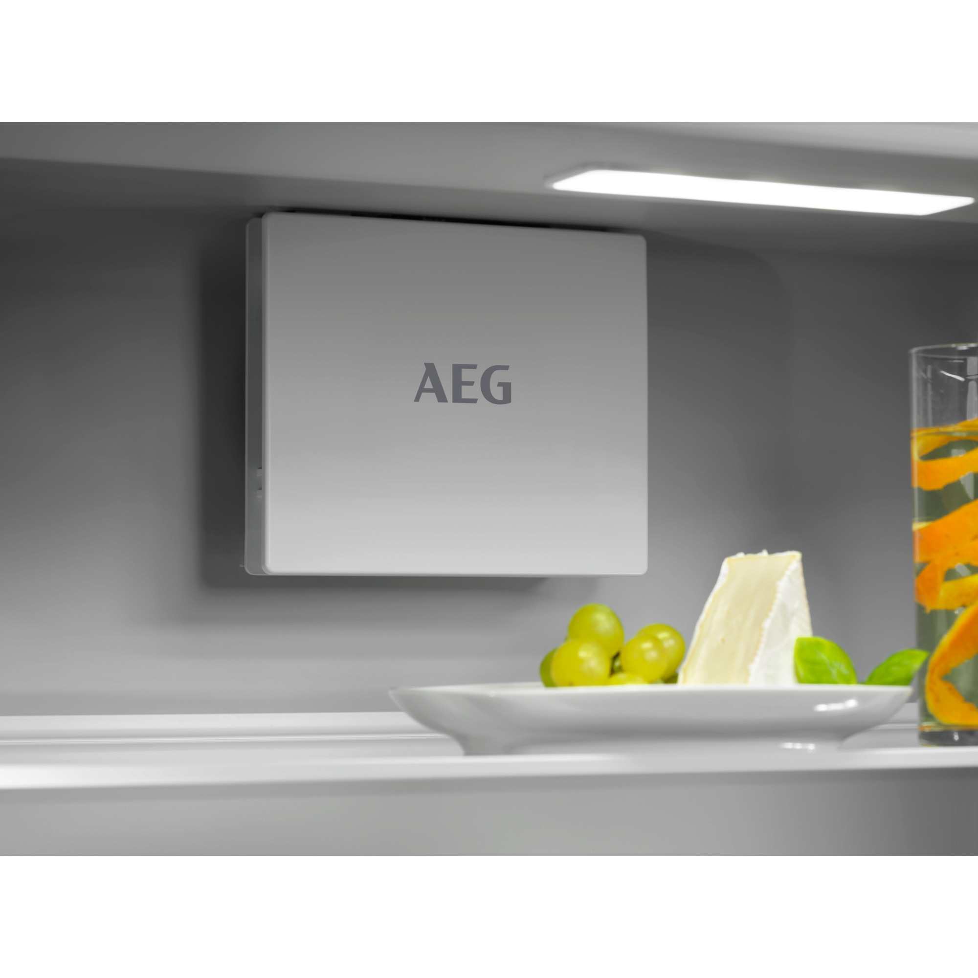 Un dispositivo AEG sobre un plato con queso, uvas y un vaso de agua con cáscara de naranja.