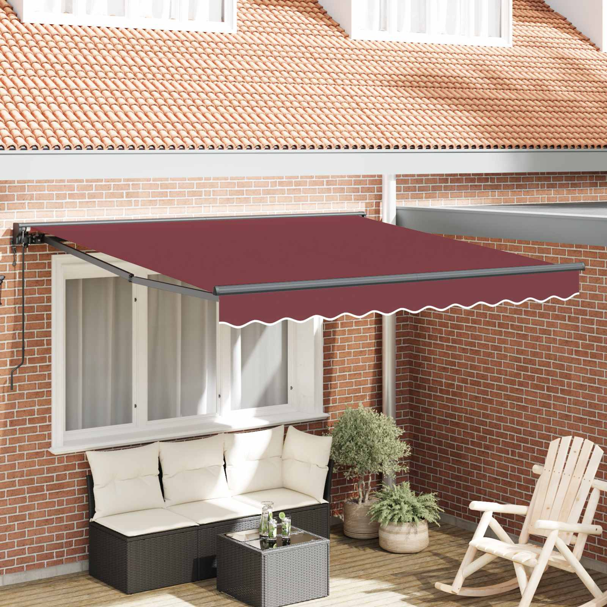 Eine burgunderrote Markise fährt über eine Terrasse mit Korbmöbeln und einem Schaukelstuhl.