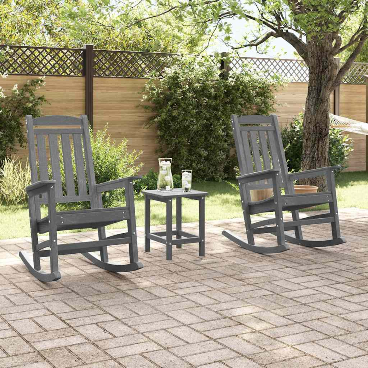 Zwei graue Schaukelstühle und ein kleiner Tisch auf einer Steinterrasse im Garten.