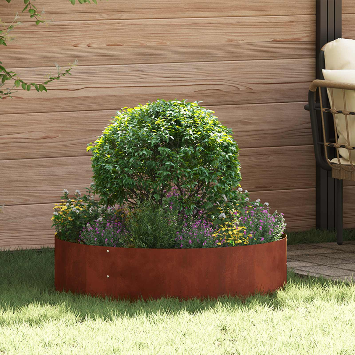Fioriera rotonda in acciaio Corten con arbusto e fiori sull'erba.