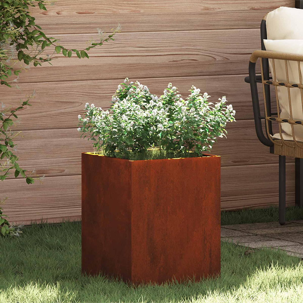 Rostiger Metallkasten mit weißen Blumen auf Gras vor Holzwand.