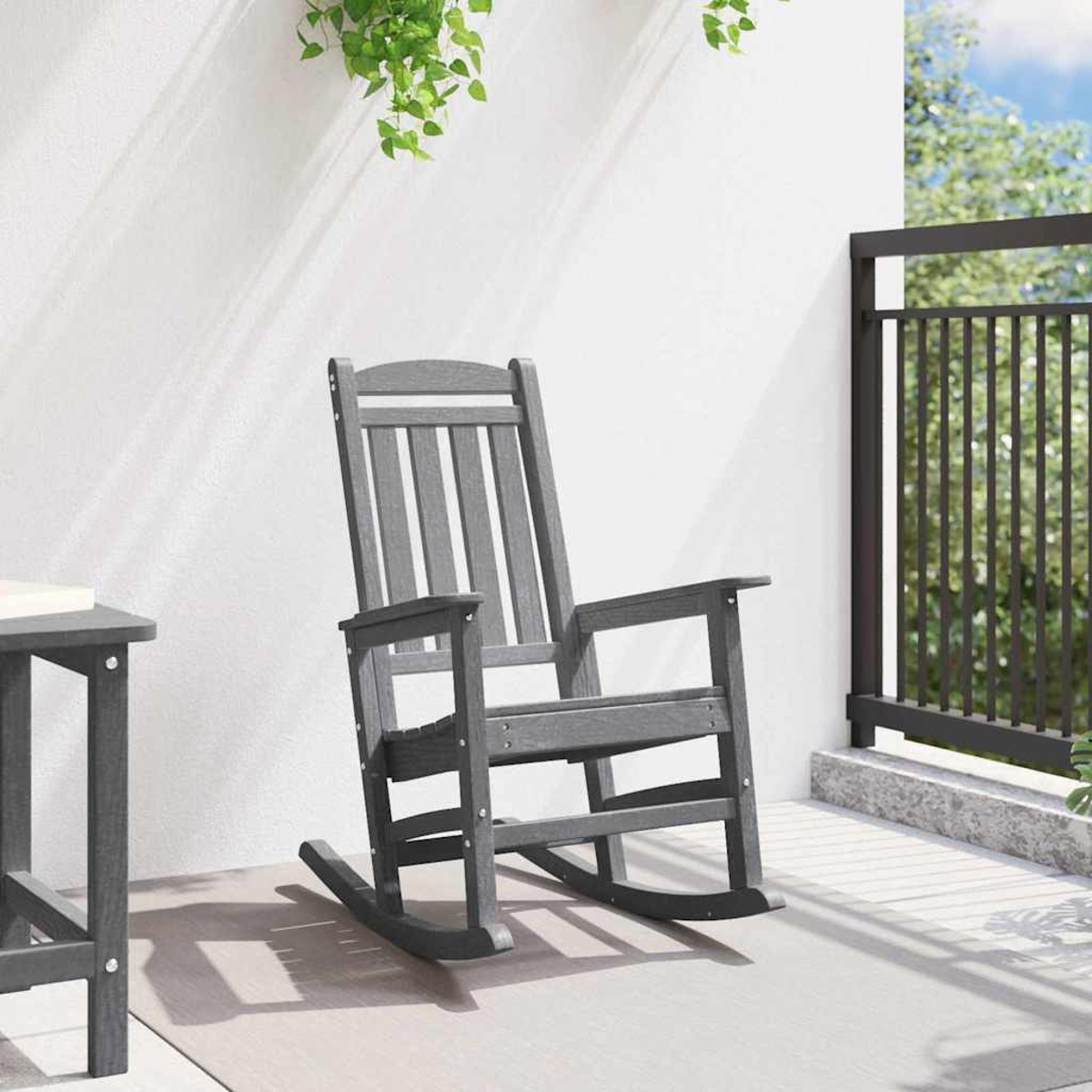 Grauer Schaukelstuhl auf einer Veranda mit einem Tisch daneben und einer Metallbalustrade.