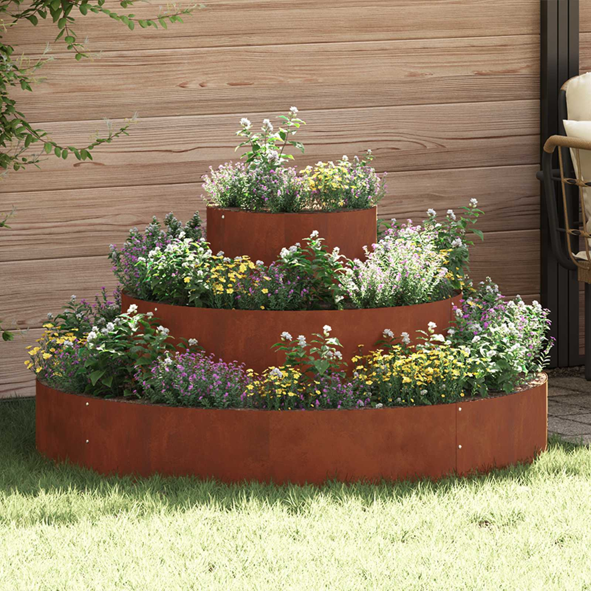 Gestufter Cortenstahl-Pflanzer mit bunten Blumen auf Rasen vor Holzwand.