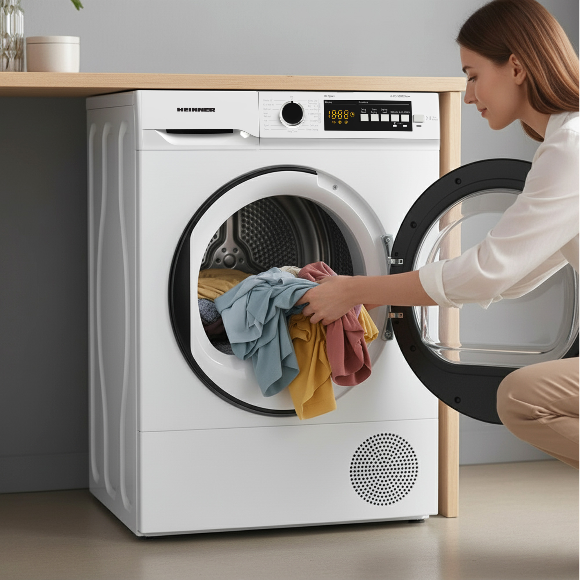 Eine Frau belädt einen weißen Wäschetrockner mit bunter Kleidung.