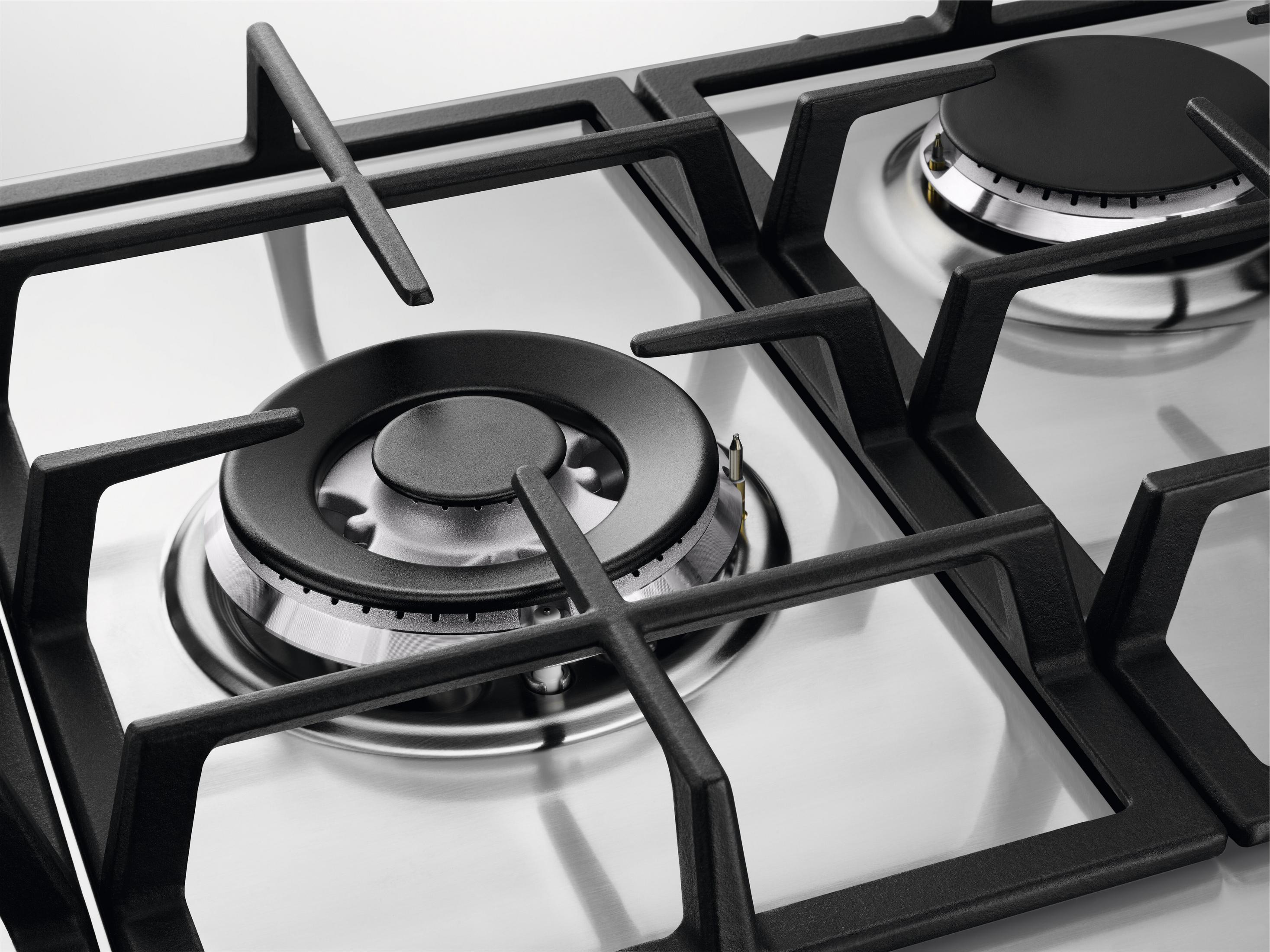 Zbliżenie kuchenki gazowej z czarnymi żeliwnymi rusztami i srebrnymi palnikami.