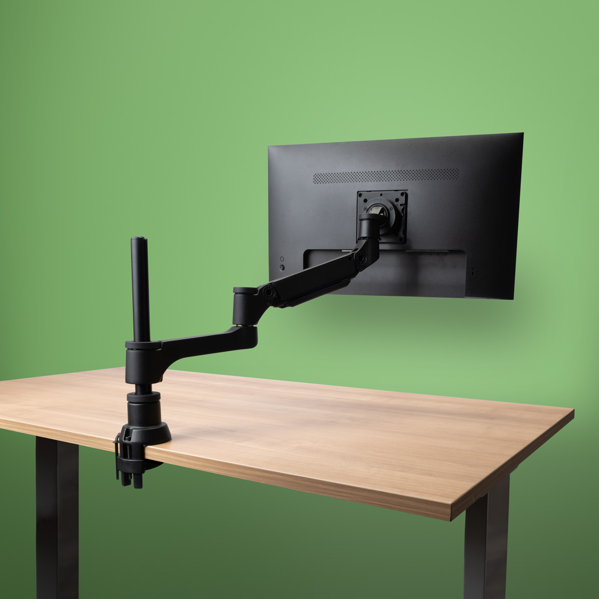 Een zwarte monitorarm is bevestigd aan een houten bureau en houdt een zwarte monitor vast.