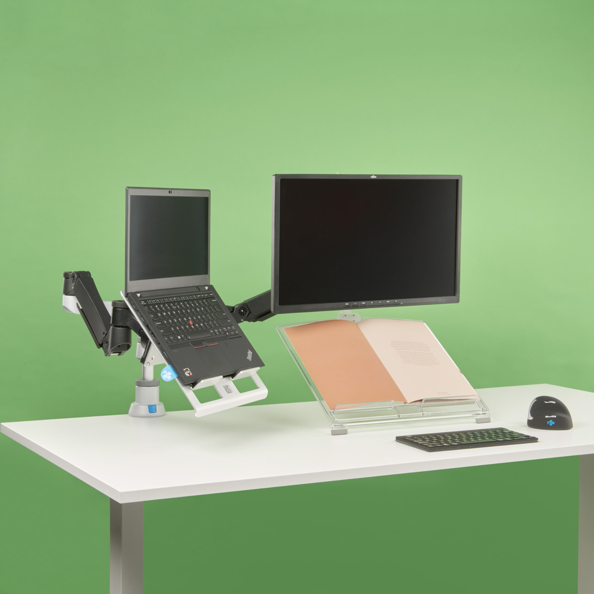 Een laptop en monitor op een bureau met een boek en muis.