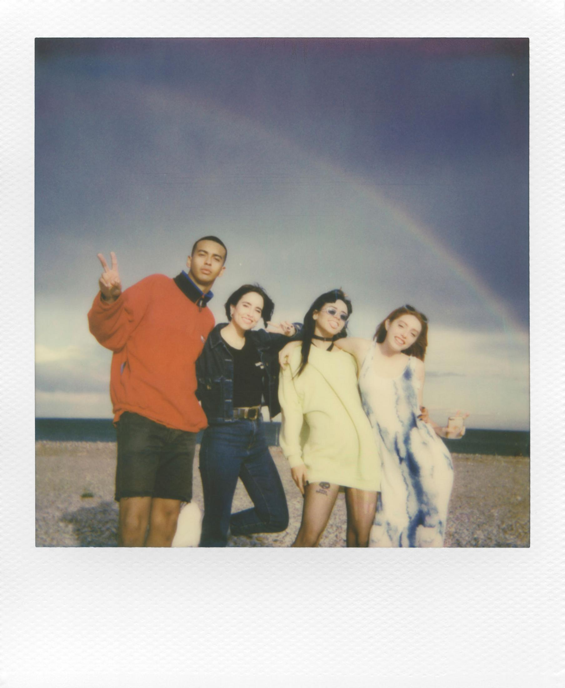 Cztery osoby stoją na plaży z tęczą na niebie.