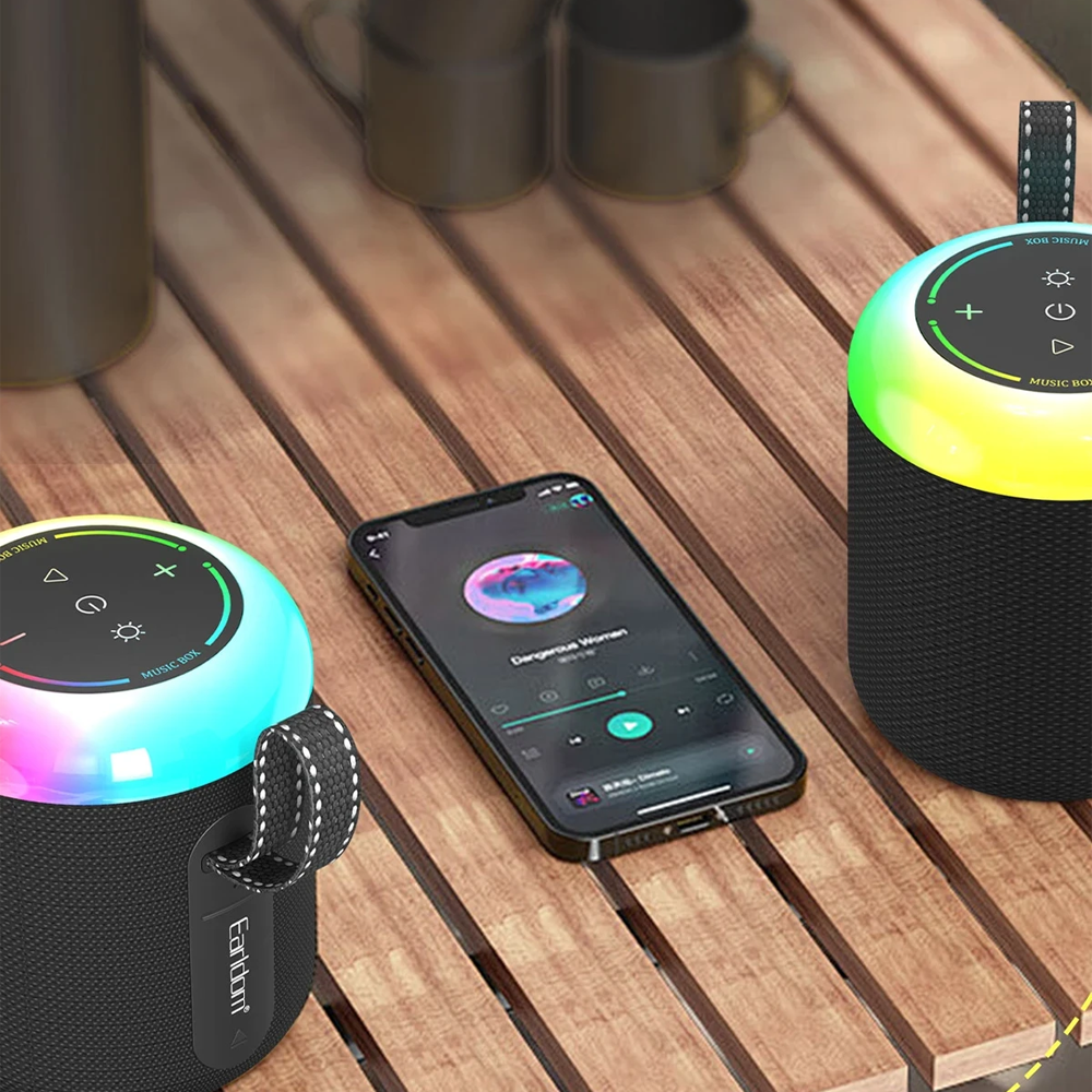Ahşap bir masada iki Bluetooth hoparlör ve bir akıllı telefon. Renkli ışıklar.