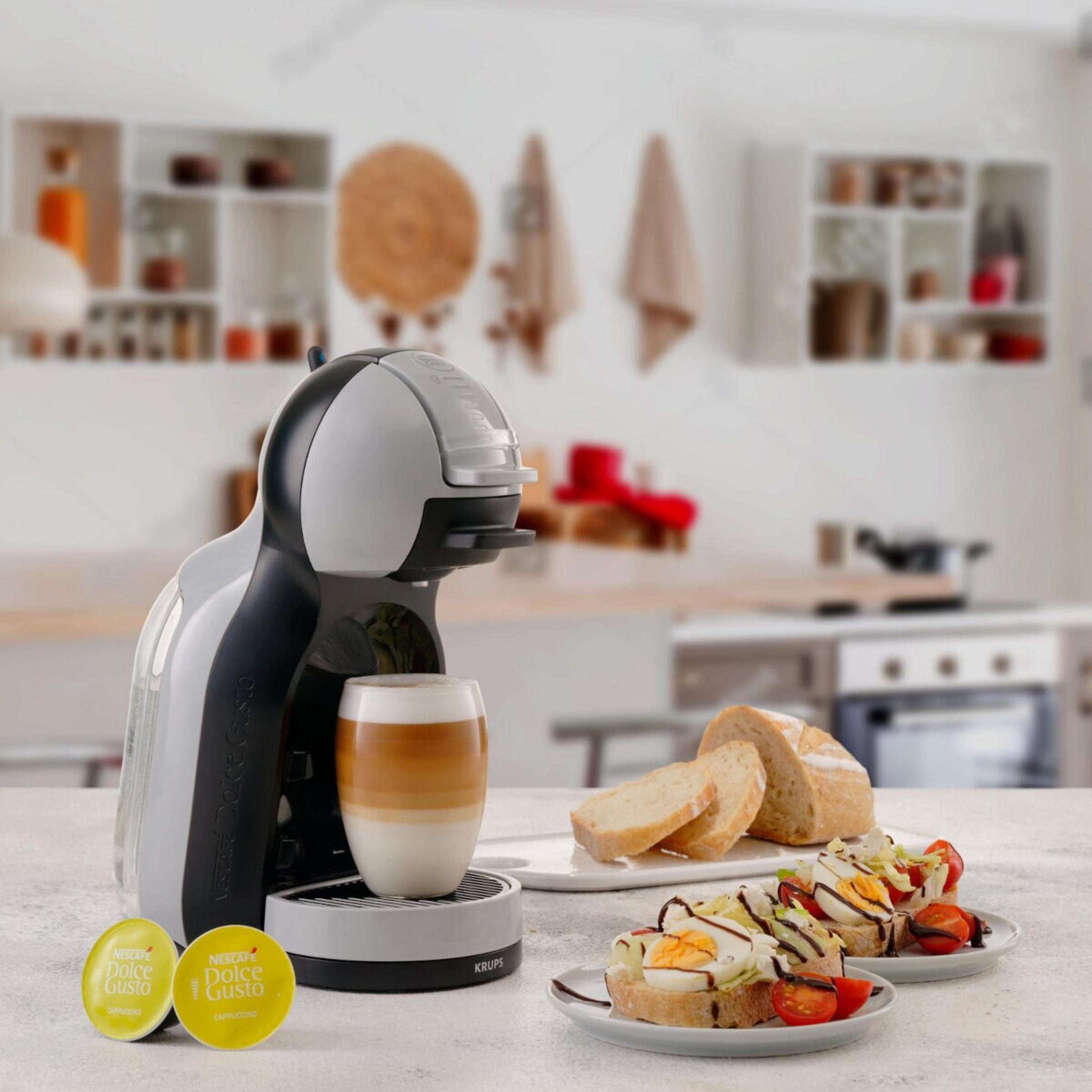 Kaffeemaschine mit Cappuccino-Glas, Brotscheiben und belegten Broten auf einem Tisch.