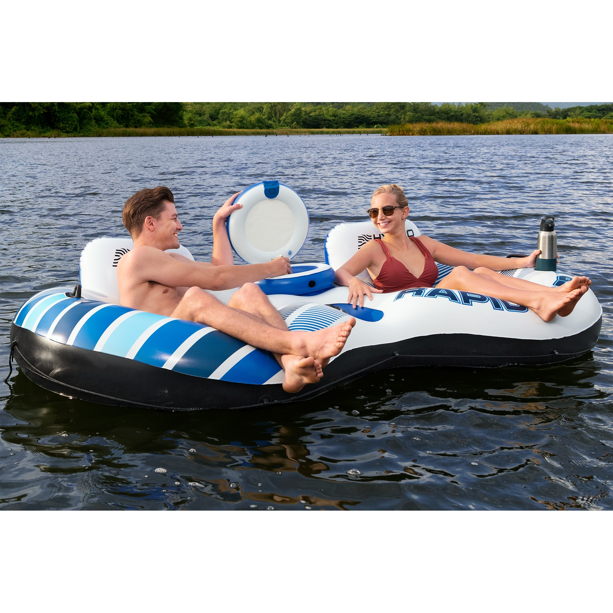 Ein Mann und eine Frau entspannen sich auf einem aufblasbaren Floß auf einem See, umgeben von Bäumen.