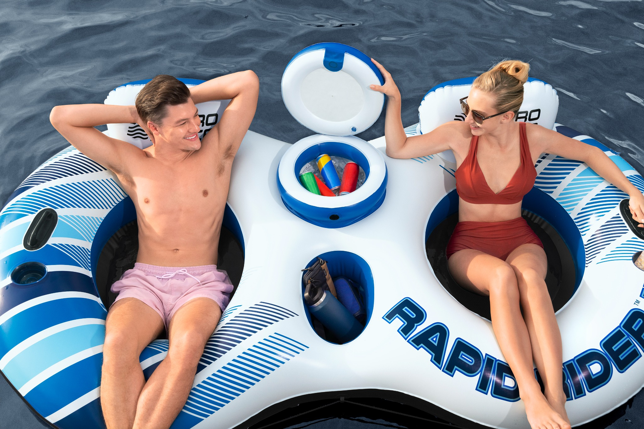 Mann und Frau entspannen sich auf einem aufblasbaren Floß im Wasser mit Getränken.