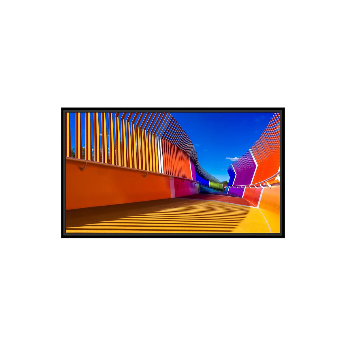 Eine bunte Brücke mit Streifenmuster und Schatten unter blauem Himmel.