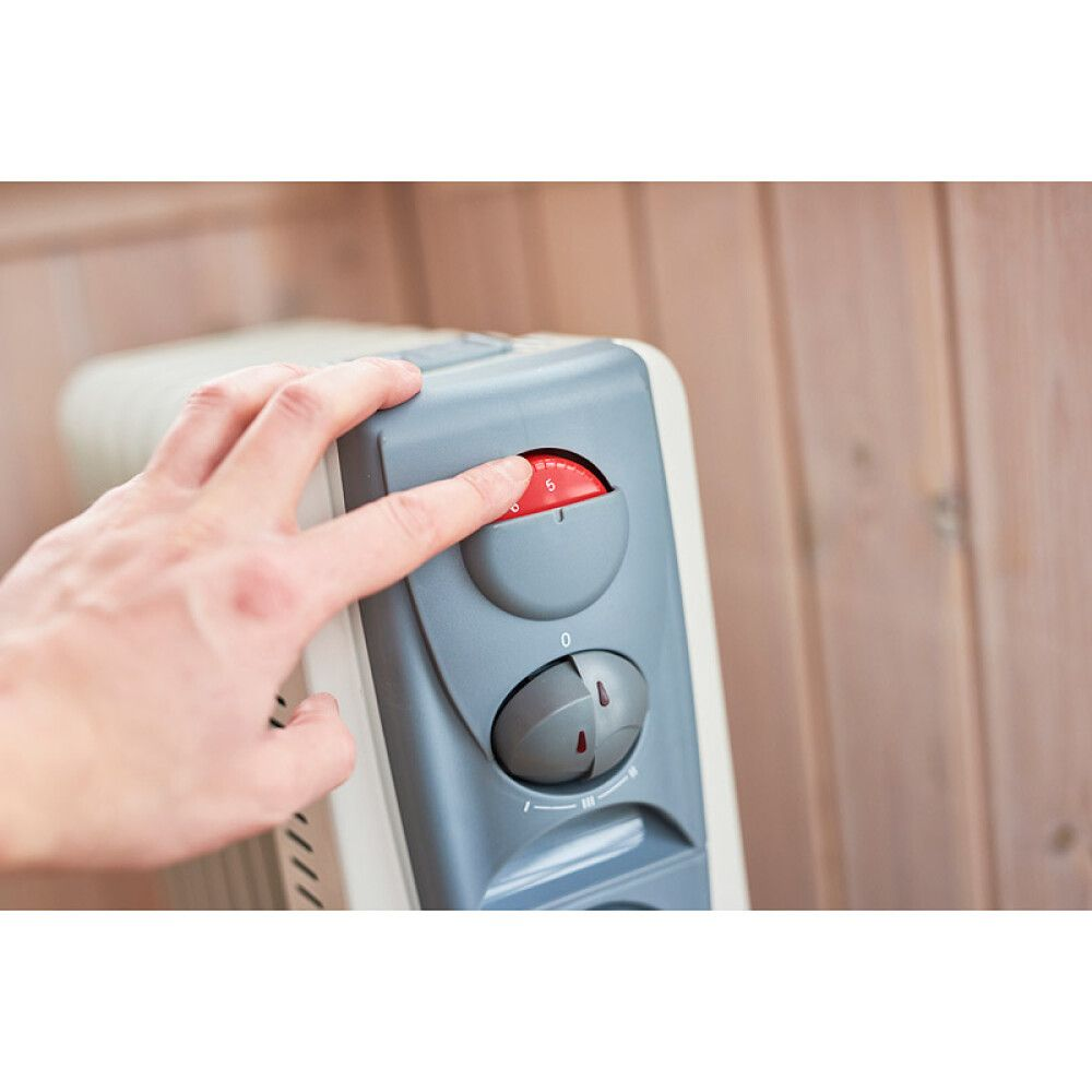 Eine Hand stellt den Thermostat eines Heizgeräts auf Stufe 5.