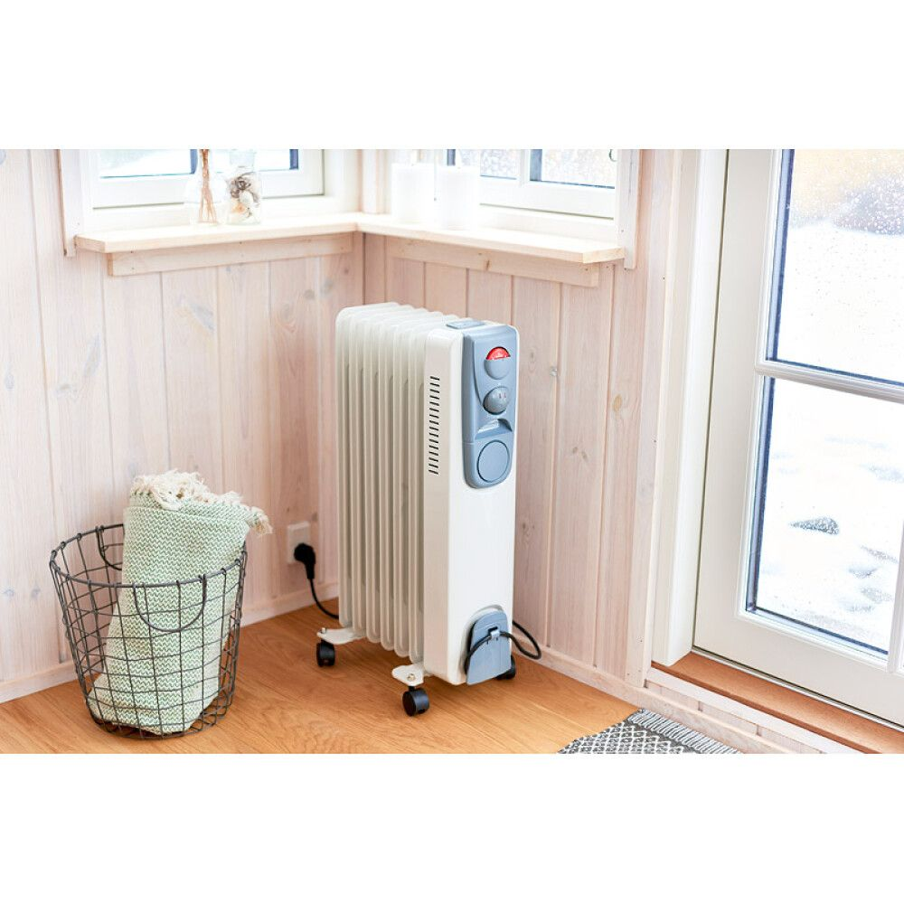 Ein weißer Ölradiator steht auf einem Holzboden neben einem Korb mit Decken.