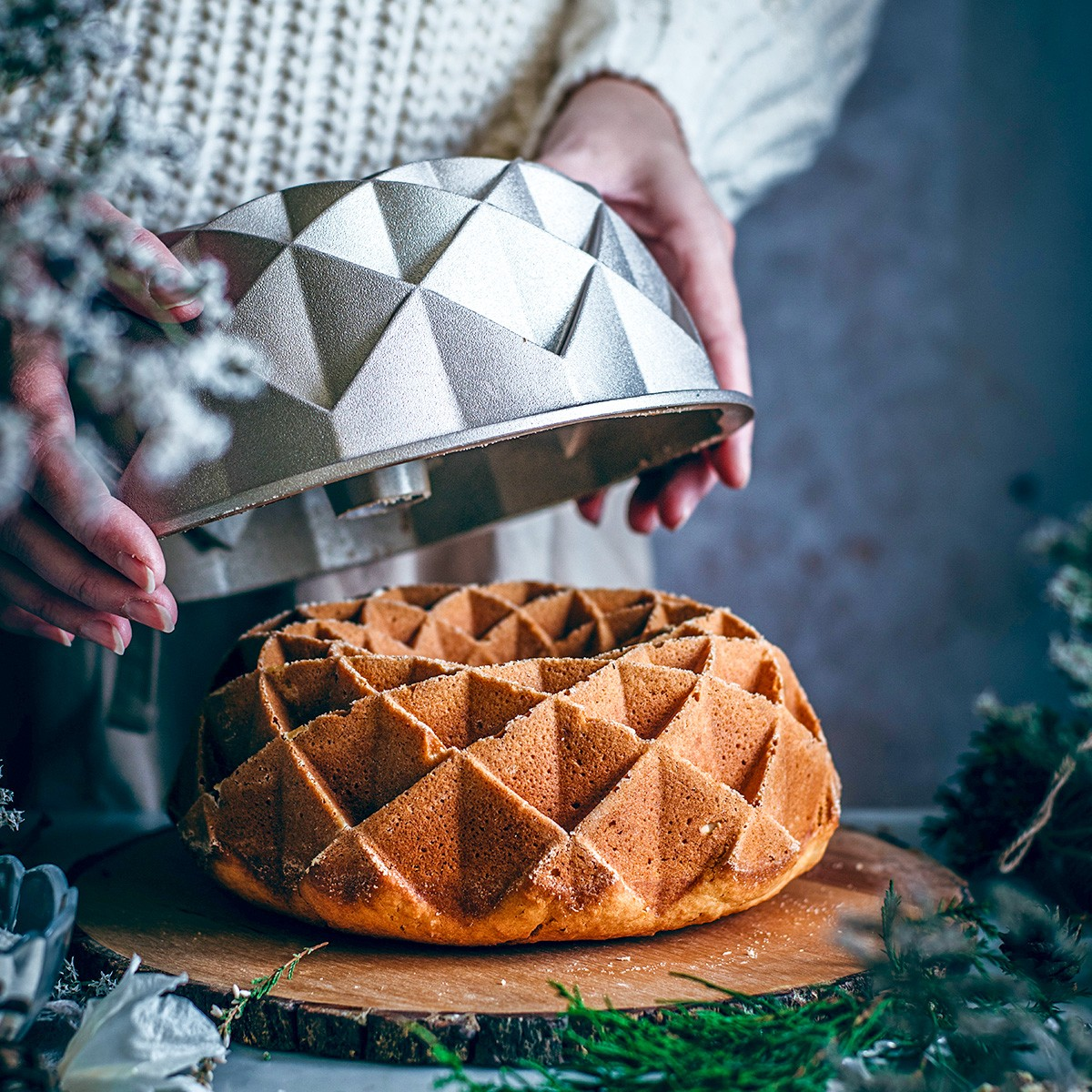 Ein diamantförmiger Kuchen wird aus einer Form gehoben. Dekoriert mit Kiefernzweigen.