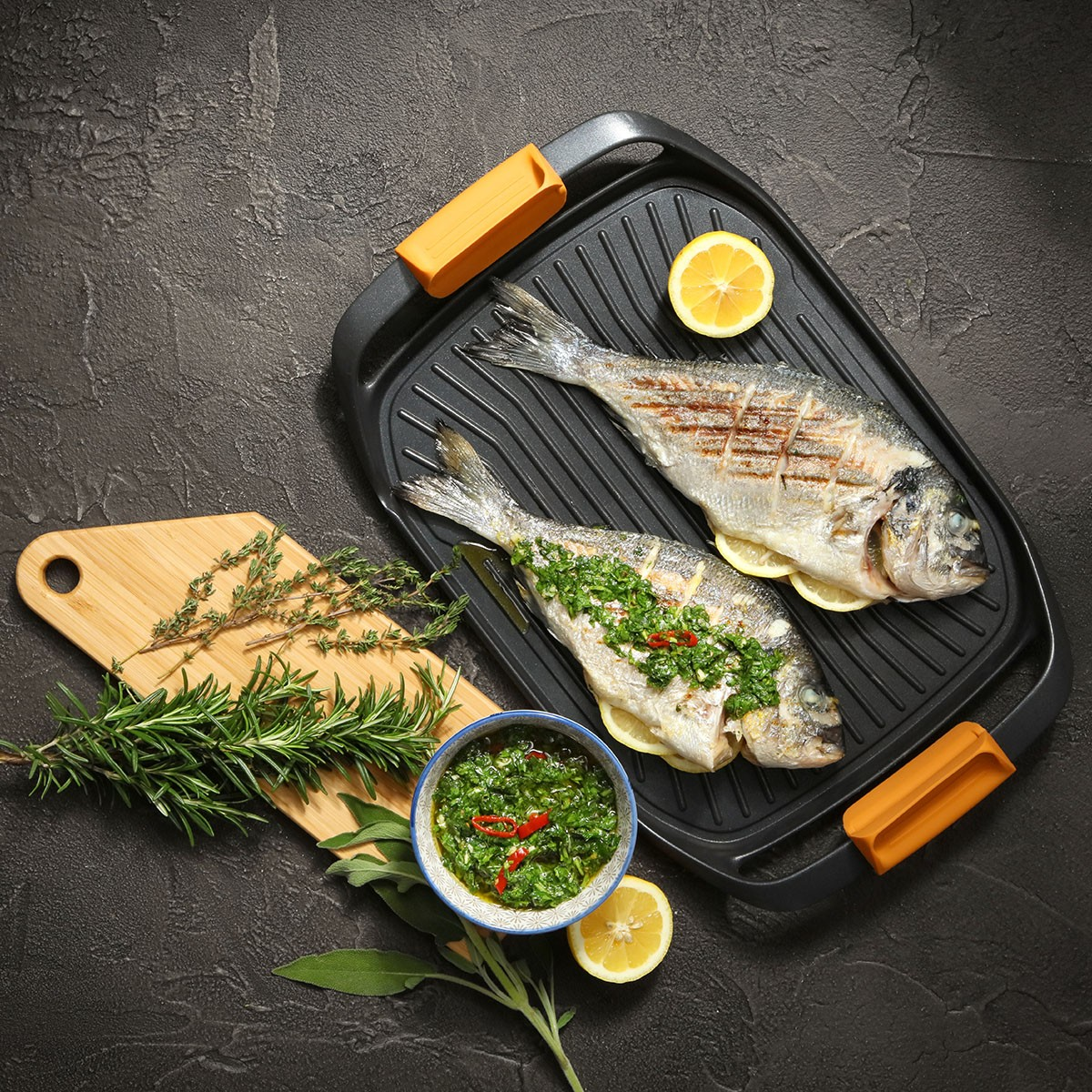 Zwei gegrillte Fische mit Kräutersauce, Zitrone und Kräutern auf Grillpfanne.