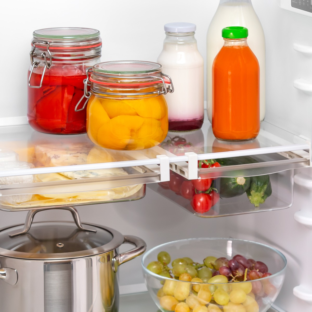 Gefüllter Kühlschrank mit Gläsern, Flaschen, Gemüse, Topf und Obstschale.