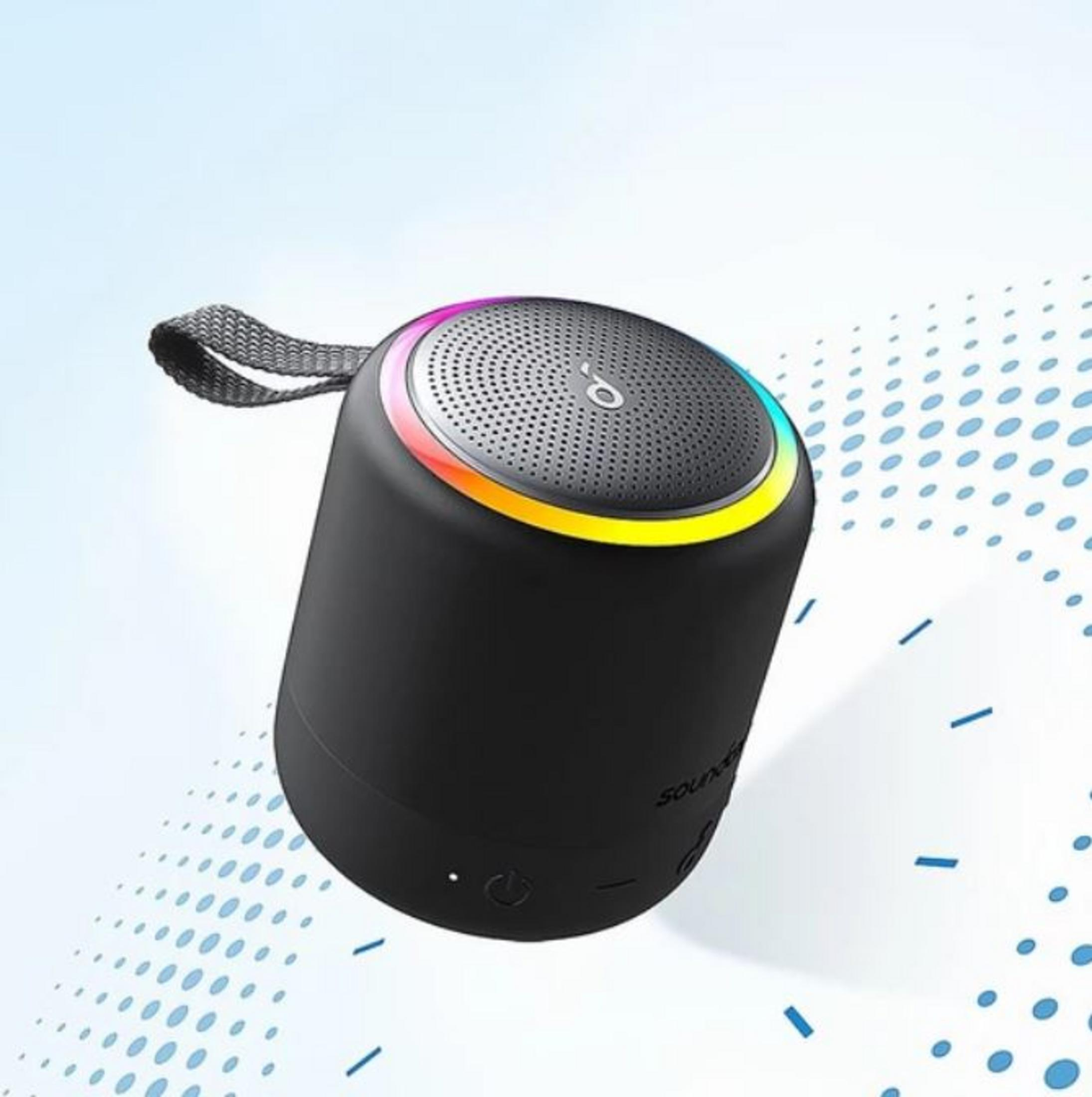Un altoparlante cilindrico nero con un anello LED colorato in cima e un cinturino grigio, fluttuante su uno sfondo a fantasia blu e bianca.