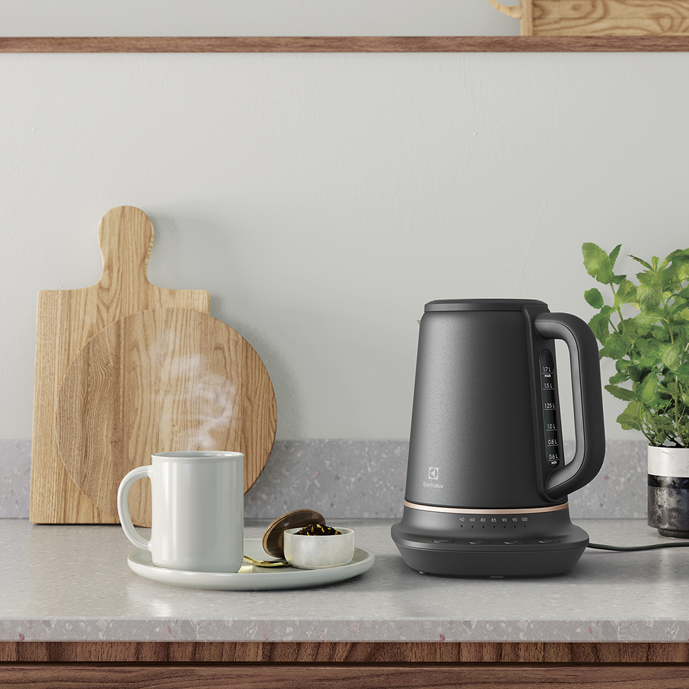 Czajnik elektryczny z filiżanką herbaty i drewnianymi deskami na blacie.