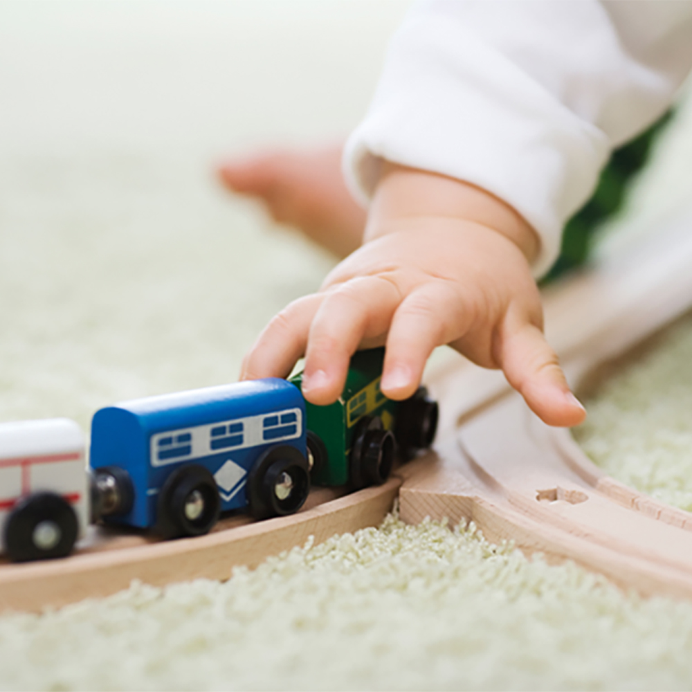 Dziecko bawi się drewnianą zabawką-kolejką na dywanie.