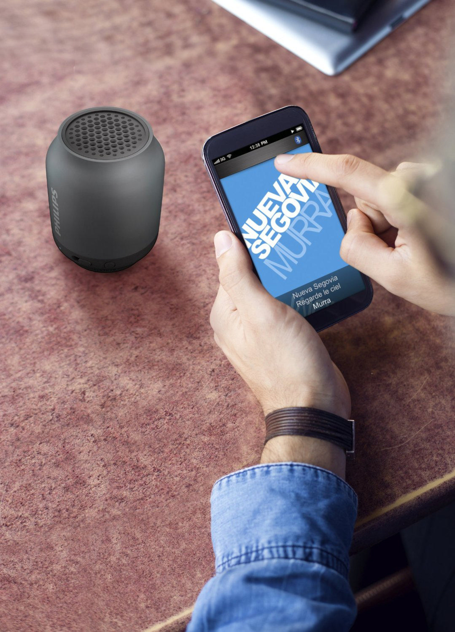 Szary głośnik obok smartfona wyświetlającego aplikację muzyczną.