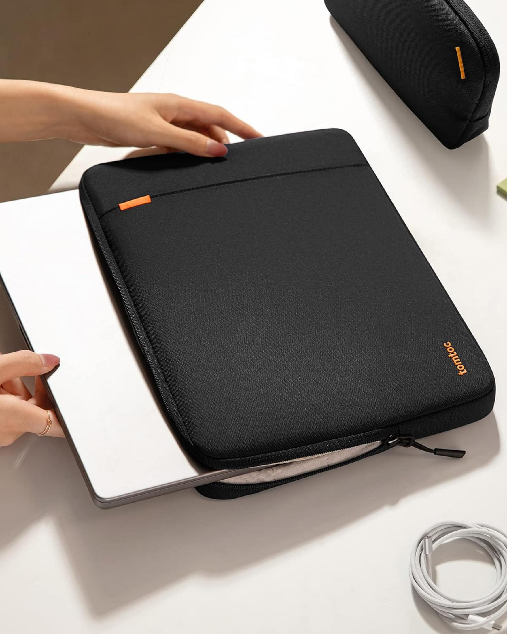 Ręka wsuwa laptopa do czarnego etui na białym stole.