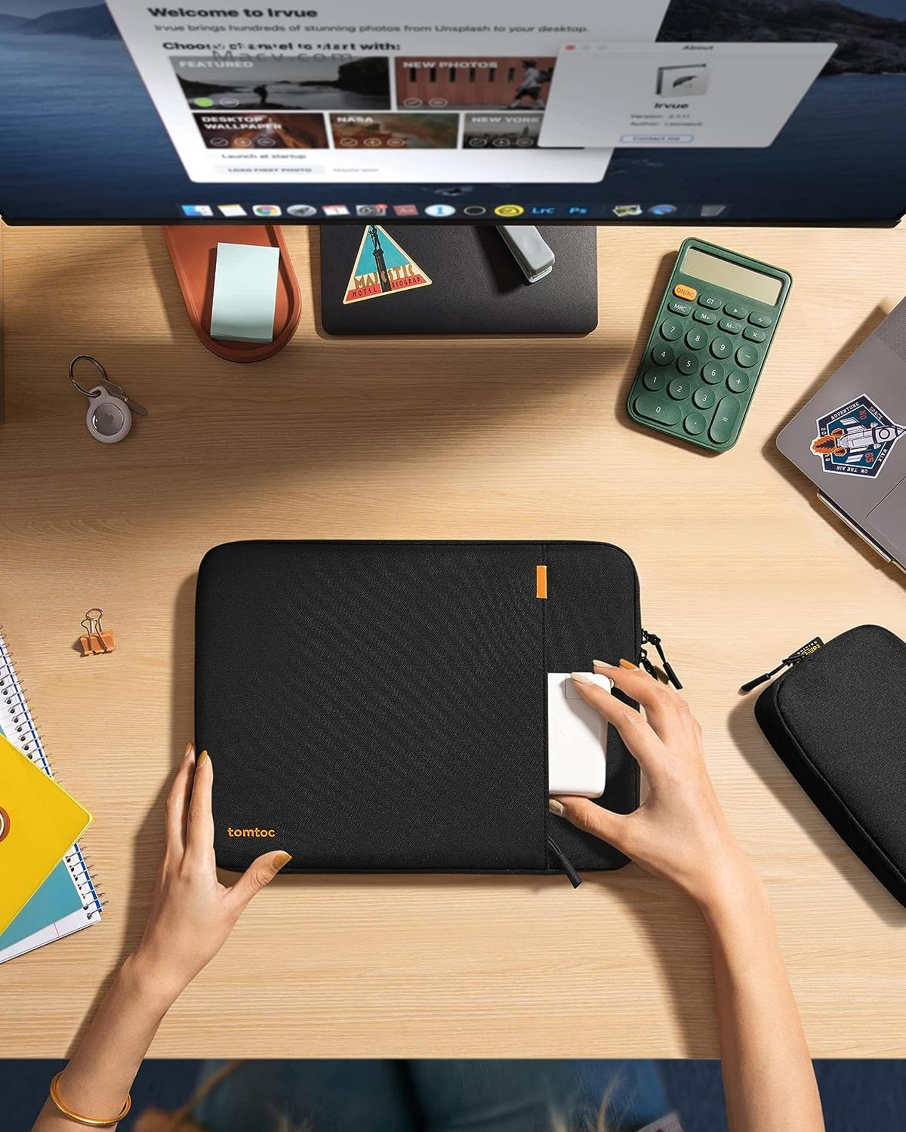 Osoba wkłada biały przedmiot do czarnej torby na laptopa na drewnianym biurku.