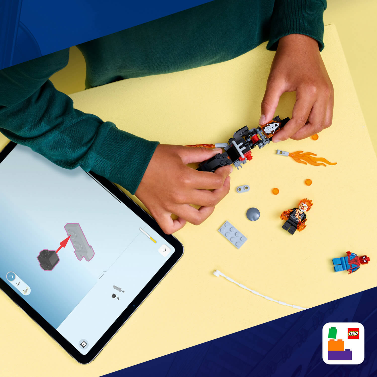 Çocuk Lego ile inşa ediyor, tablet talimatlarına bakıyor. Yakında Spiderman figürü.