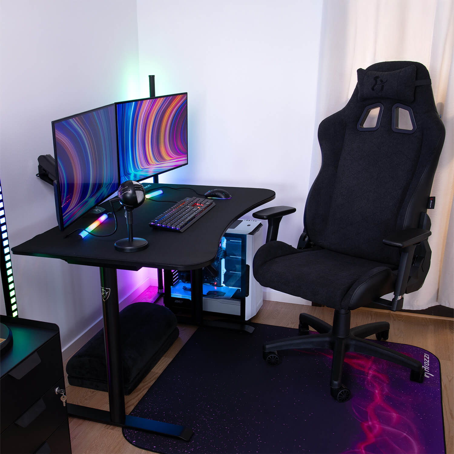Una scrivania da gaming nera con due monitor, tastiera, mouse, microfono e PC.