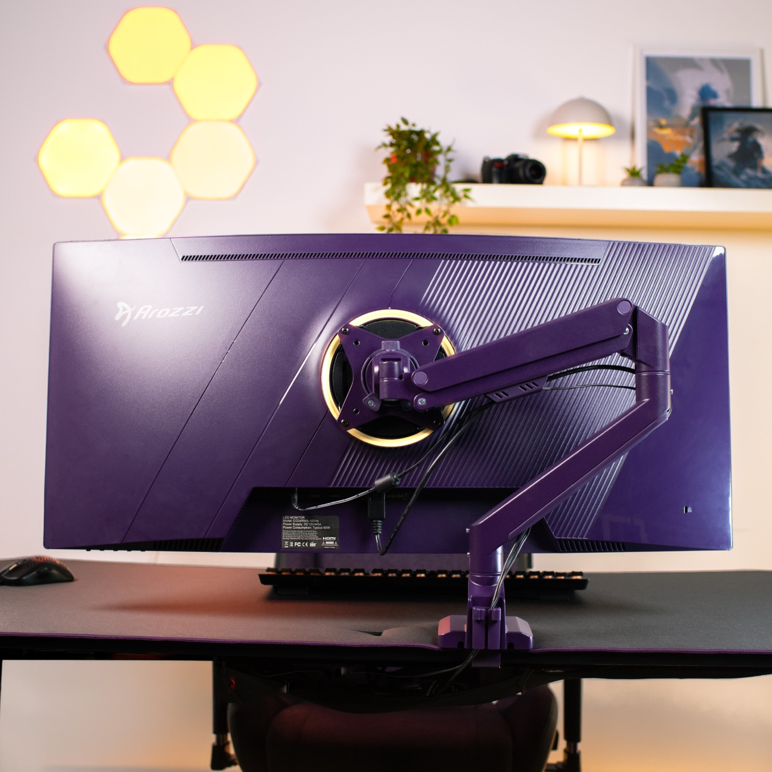 Paarse monitorachterkant met standaard, muis en toetsenbord op een bureau.
