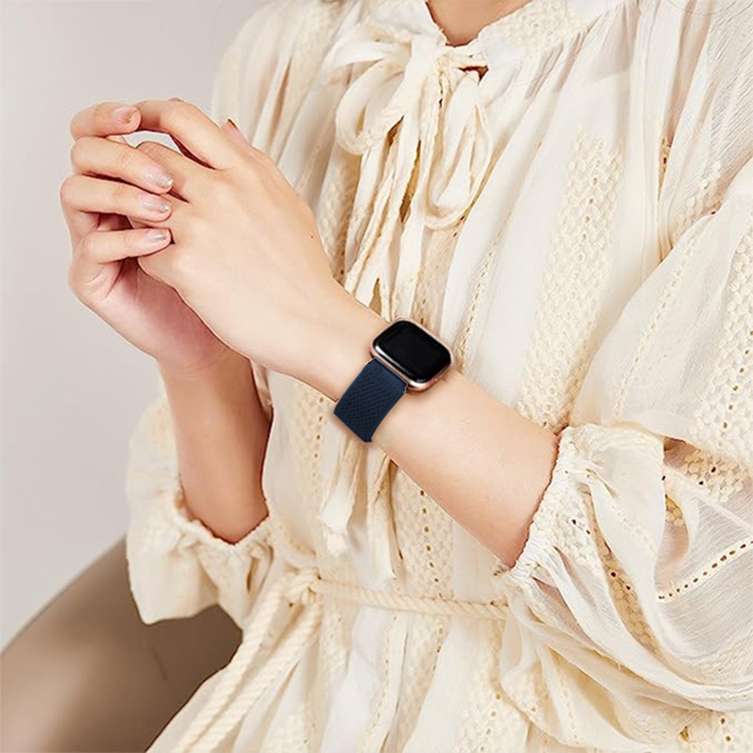 Kobieta w kremowej sukience z niebieskim smartwatchem.