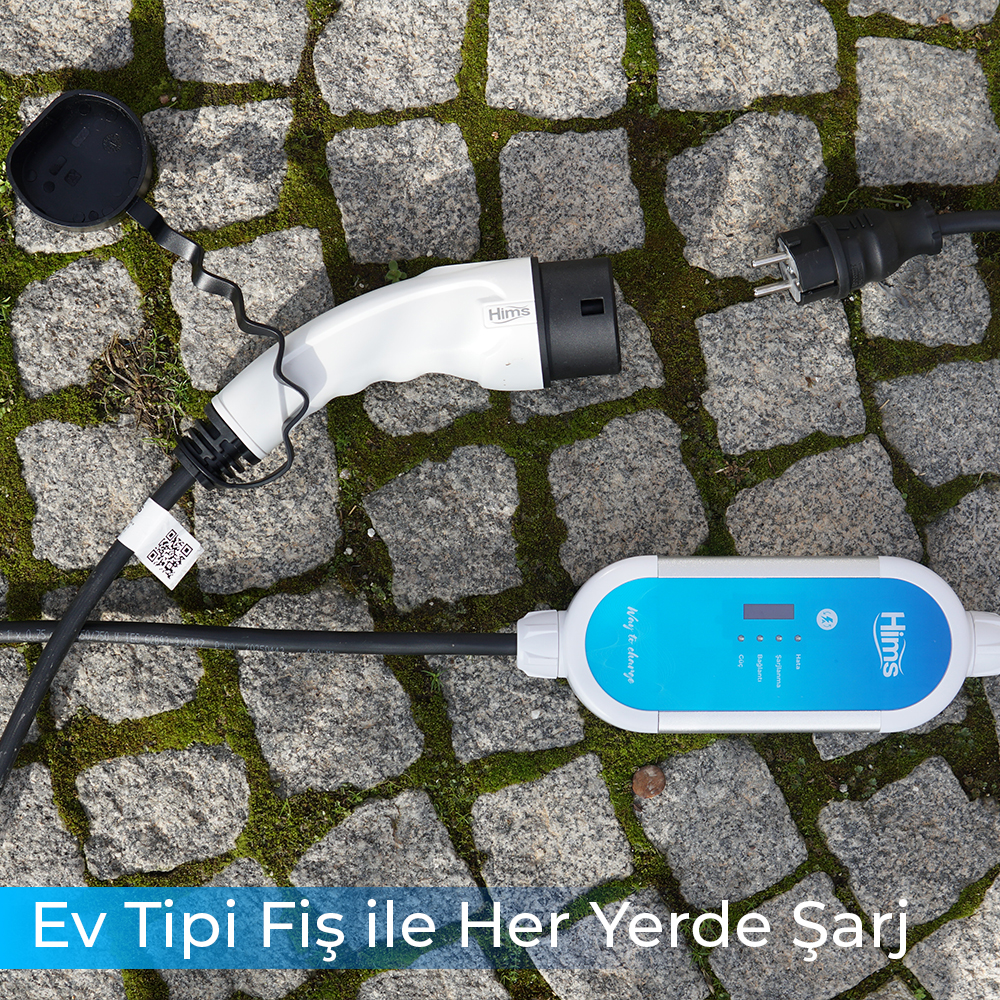 Beyaz elektrikli araç şarj cihazı ve kabloları, Arnavut kaldırımlı zeminde.